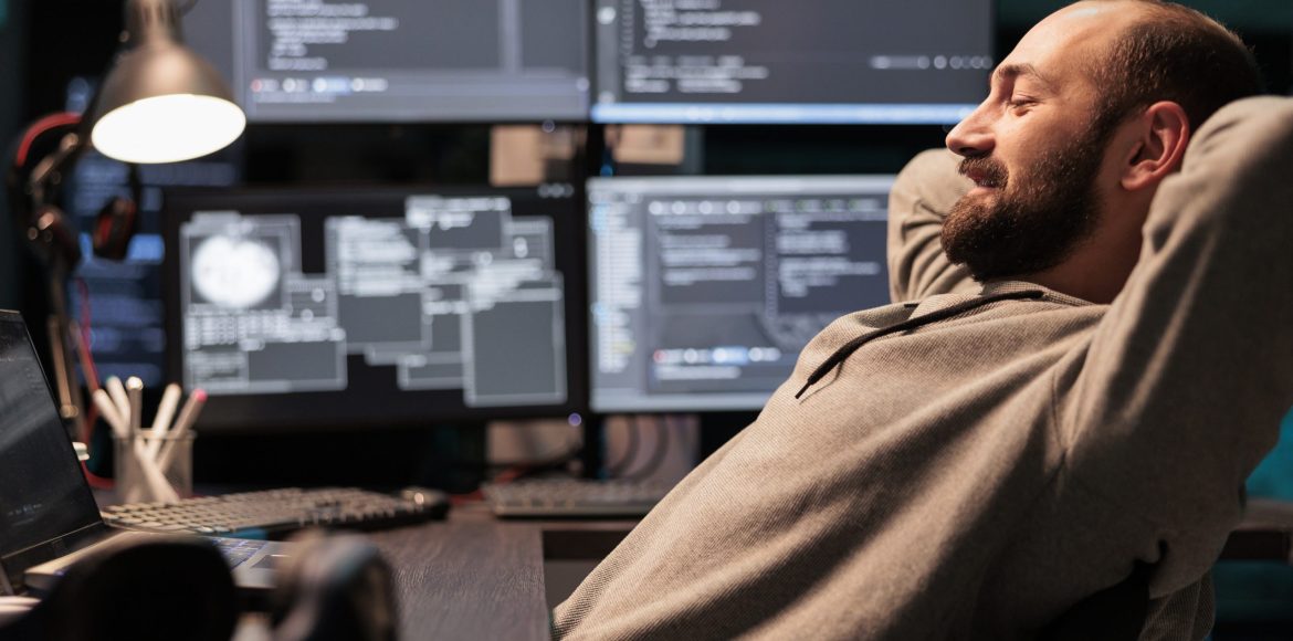 Smiling relaxed coder sitting laid back on chair, feeling pleased about software development work in office. Enjoying server programming success late at night, server code html script.