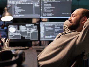 Smiling relaxed coder sitting laid back on chair, feeling pleased about software development work in office. Enjoying server programming success late at night, server code html script.